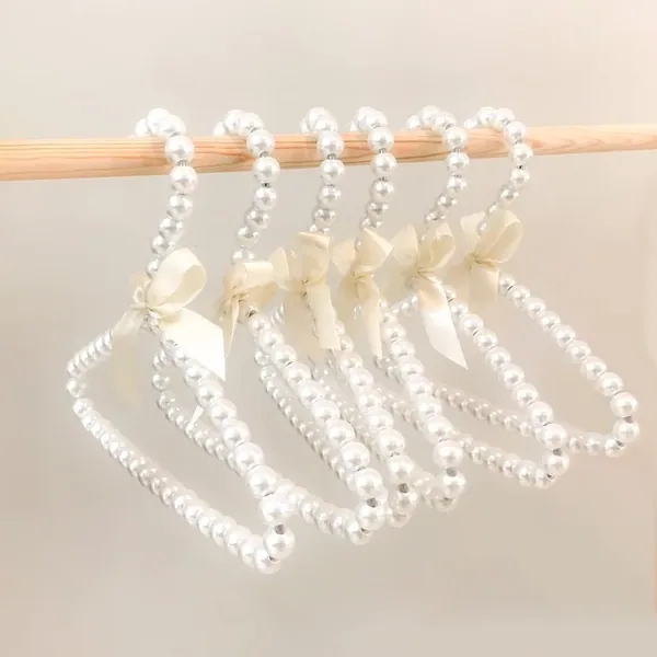 Small ivory pearl beaded kids hangers with satin bows on a wooden rail